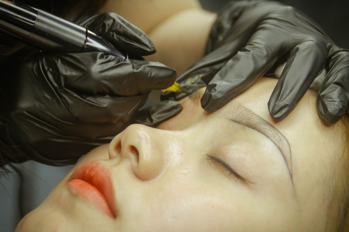 A practitioner applying permanent eyebrow makeup with gloved hands